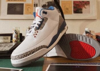Air Jordan 3 "True Blue" IF4396-104 white leather sneaker with True Blue accents, cement grey elephant print, and red Jumpman detailing, displayed on a wooden desk