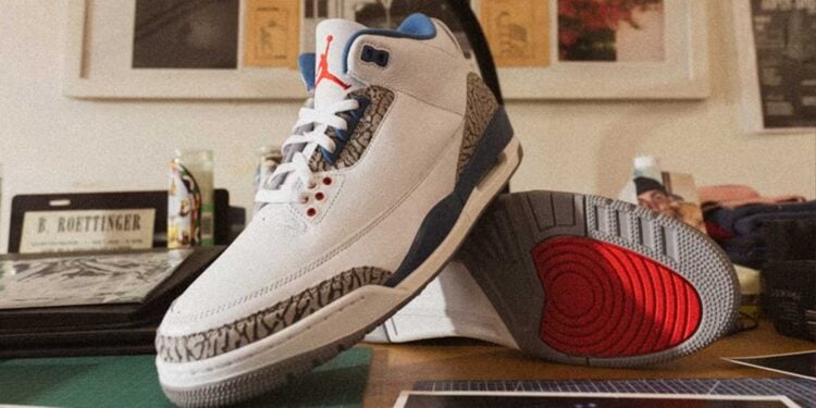 Air Jordan 3 "True Blue" IF4396-104 white leather sneaker with True Blue accents, cement grey elephant print, and red Jumpman detailing, displayed on a wooden desk